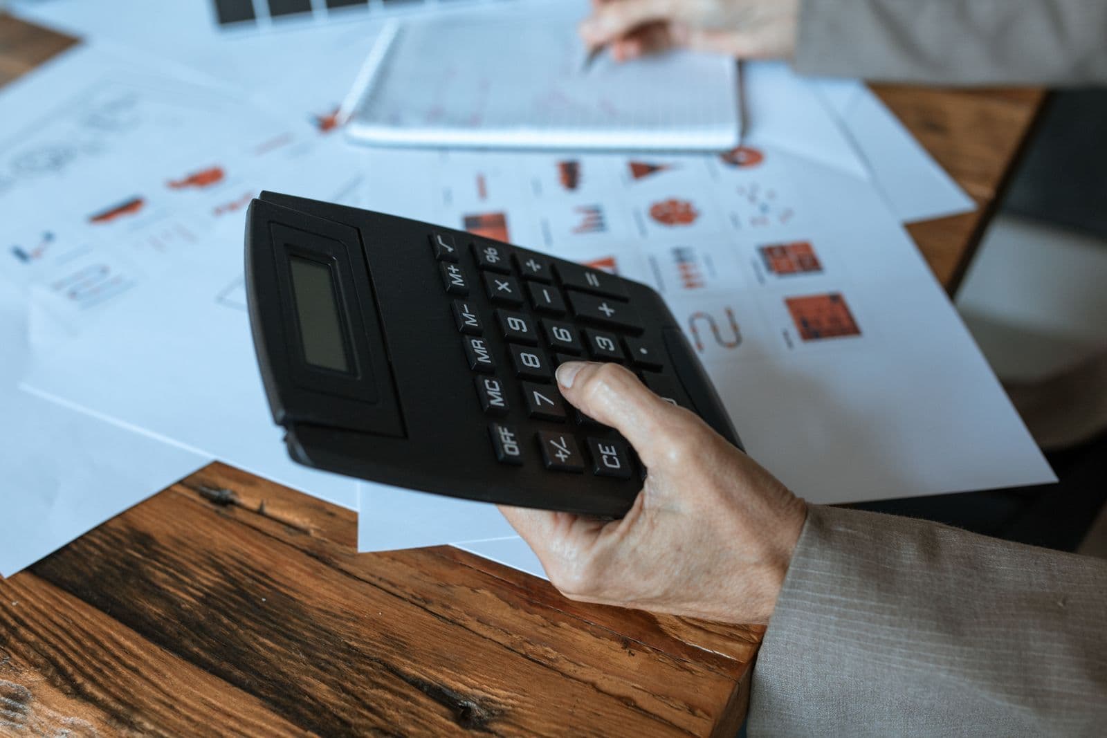 Hand using a calculator beside printed charts