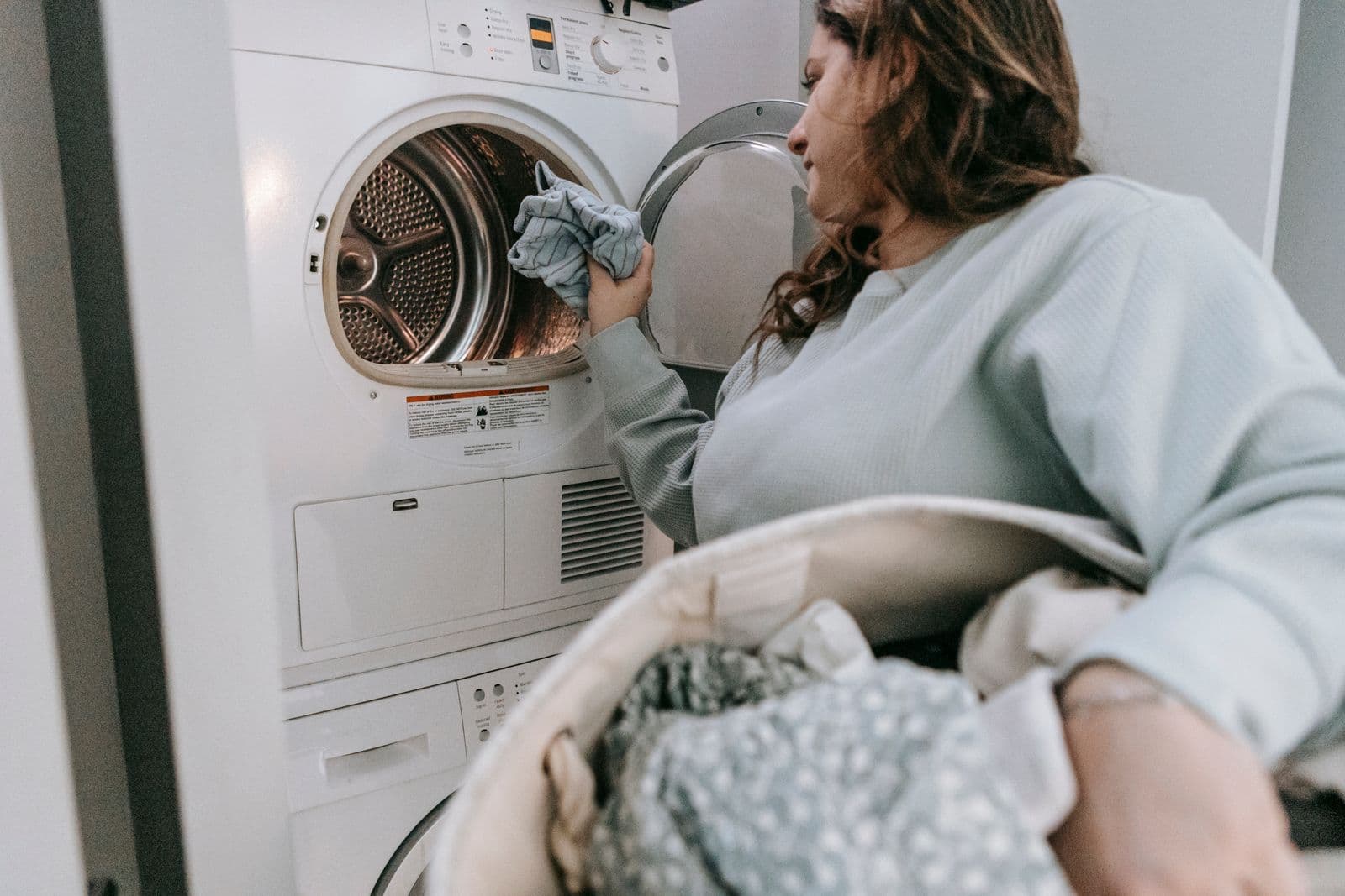 A woman loading a tumble dryer above a washing machine at home