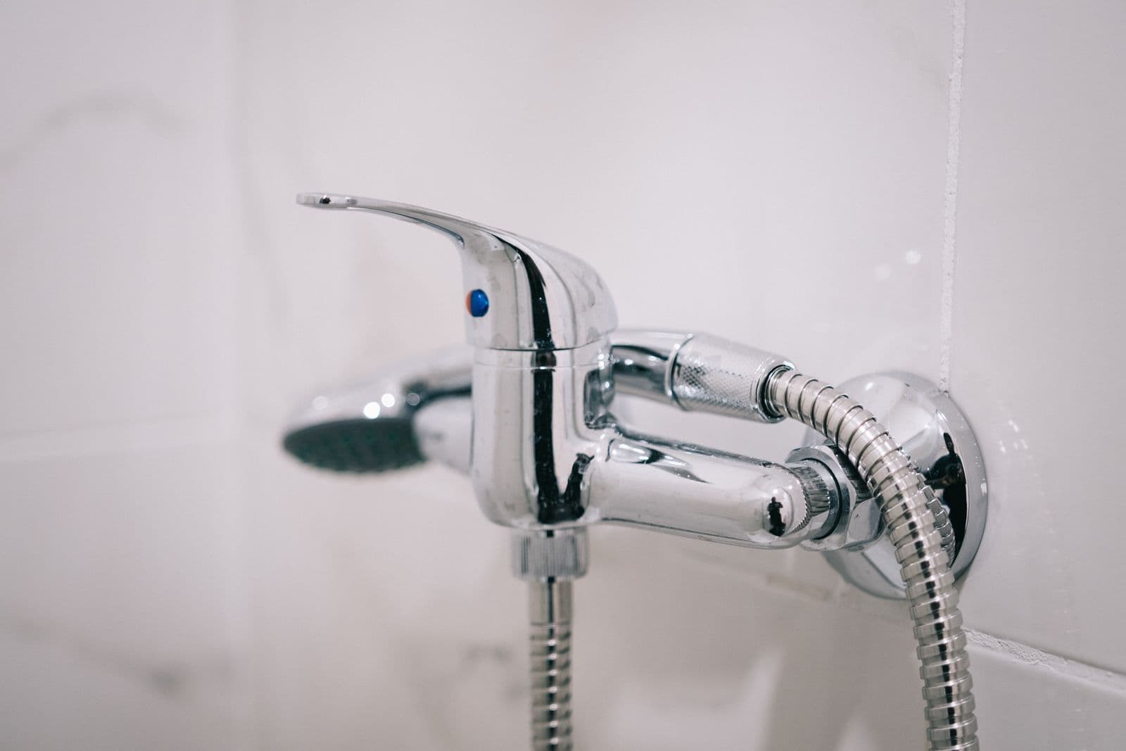 A chrome shower mixer and hose against bathroom tiles
