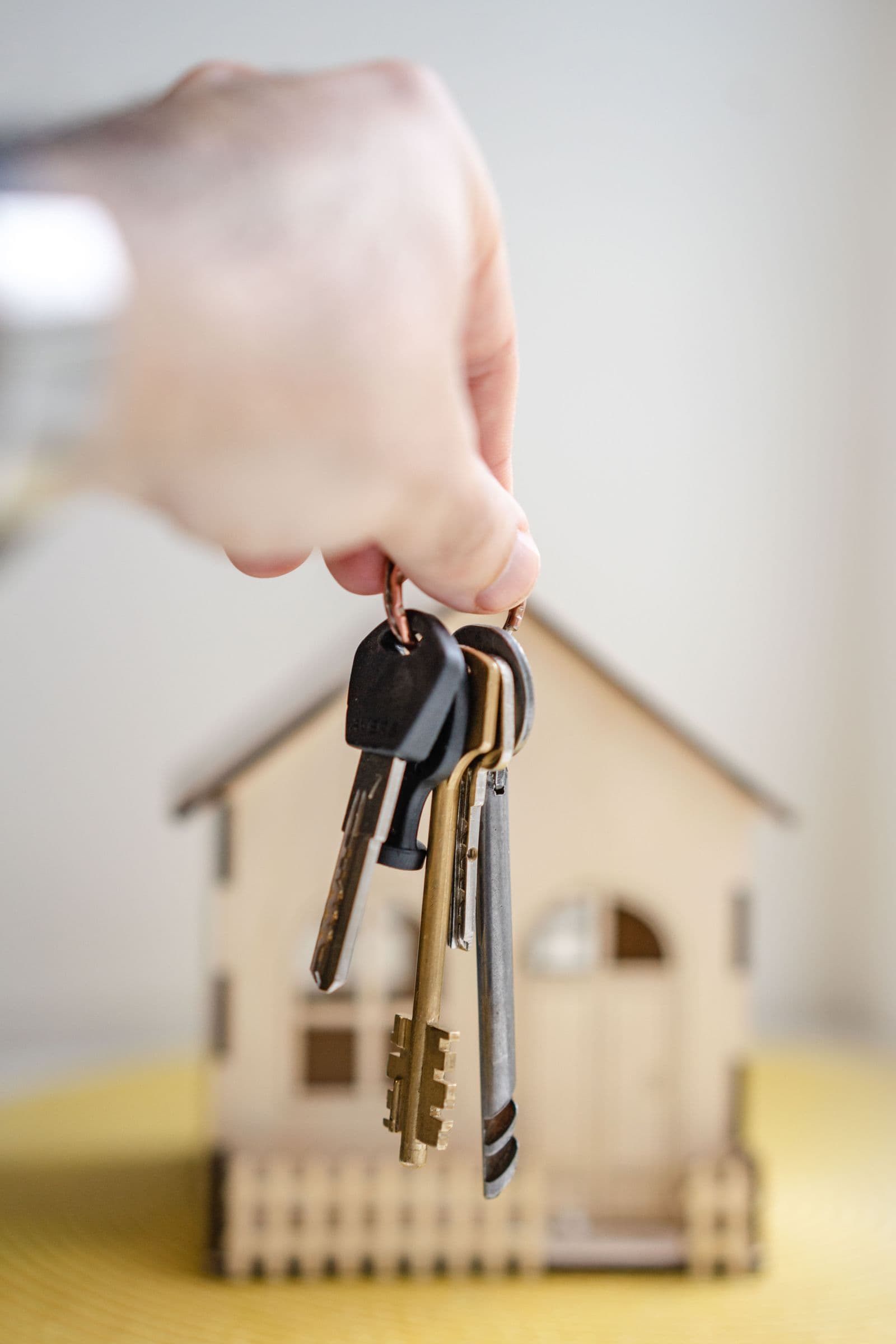 A hand holding house keys beside a small wooden house model