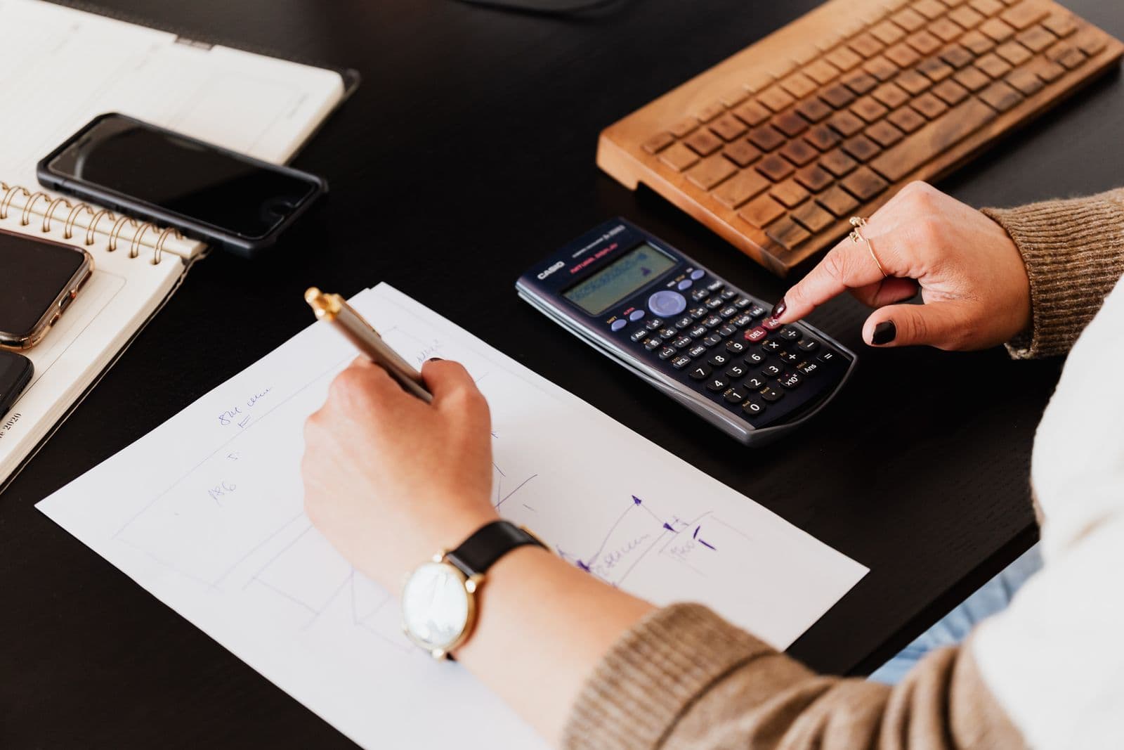 Hands using a calculator and writing figures on paper