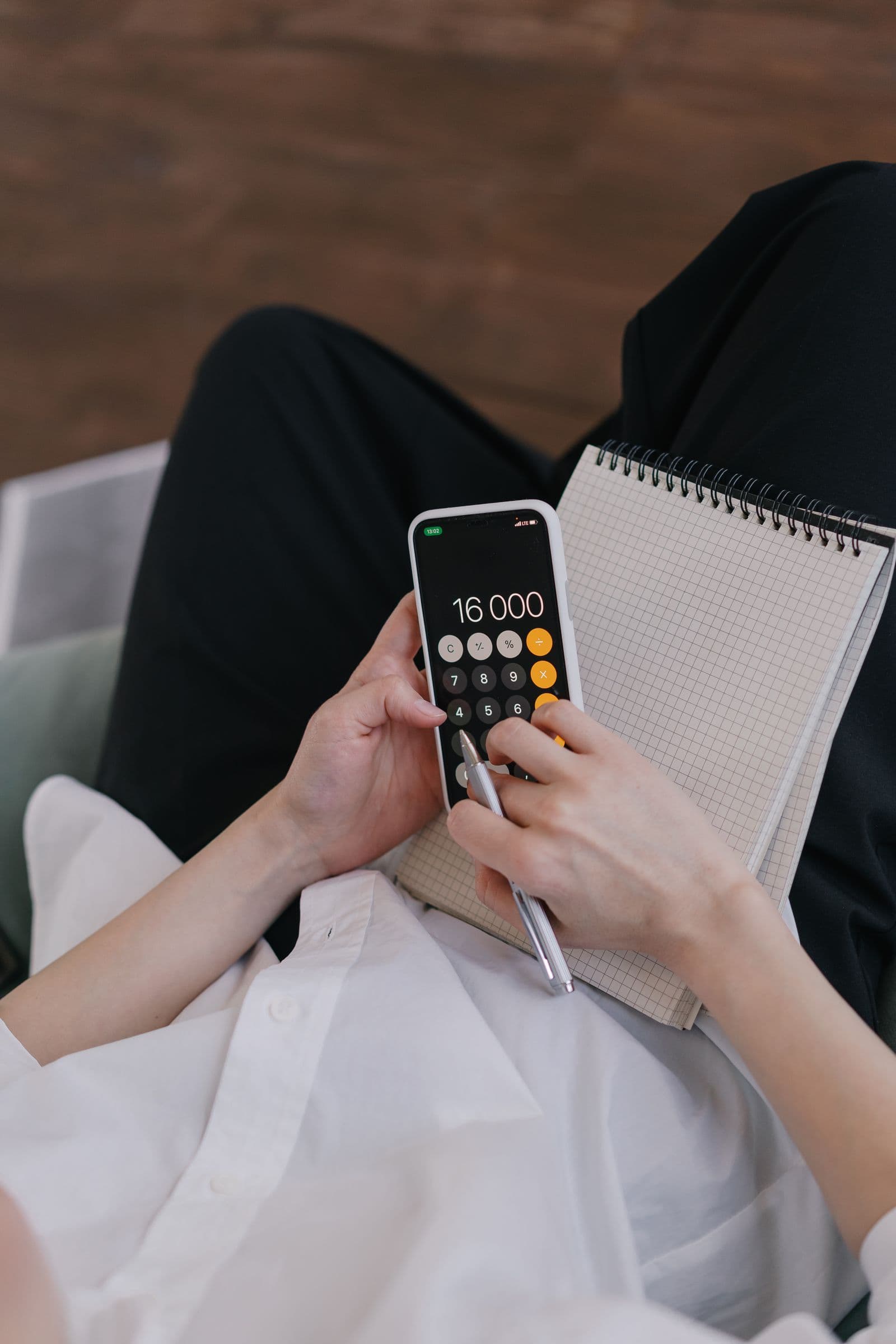 Hands using a phone calculator beside a notebook