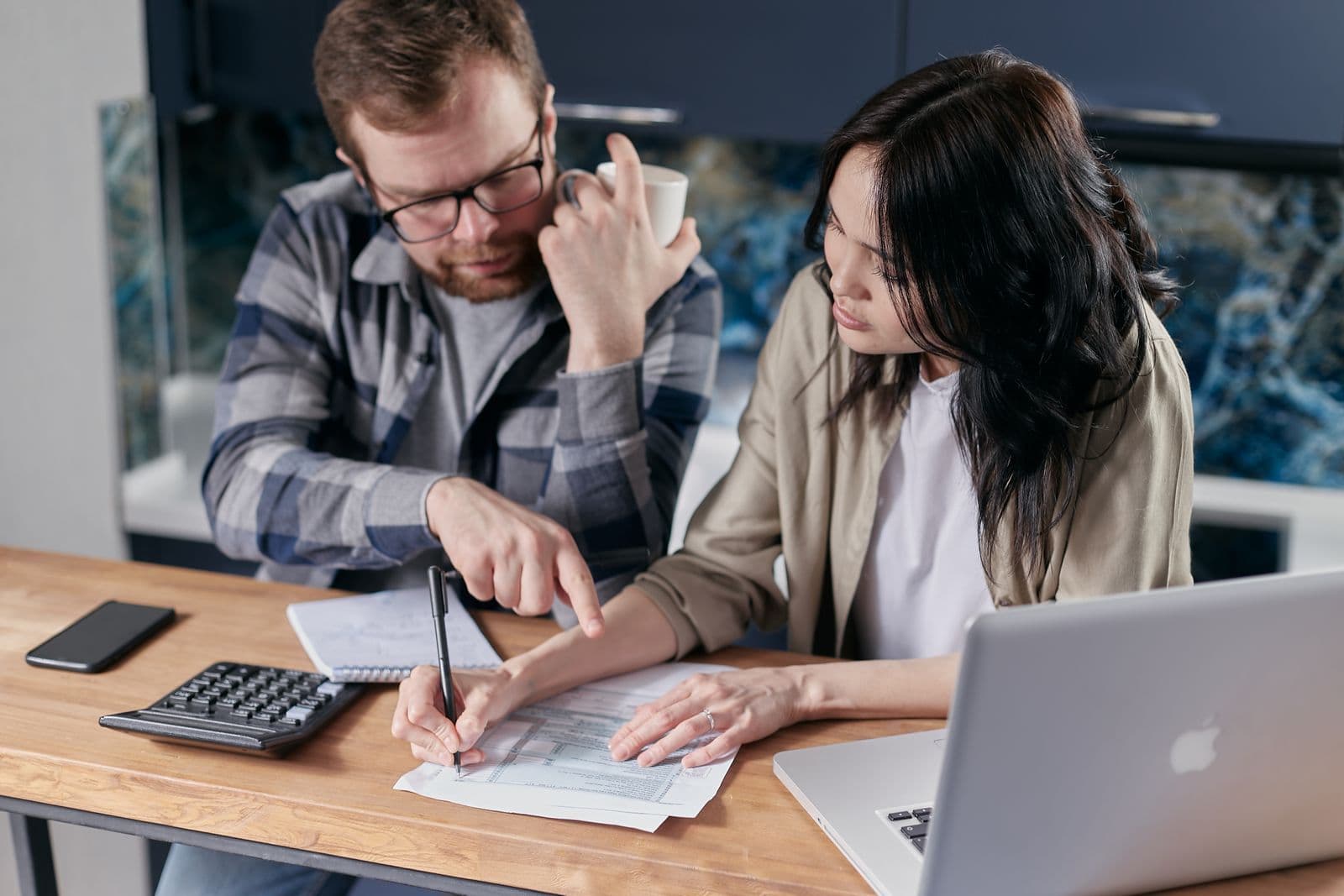 Two people comparing paperwork with a calculator at a table