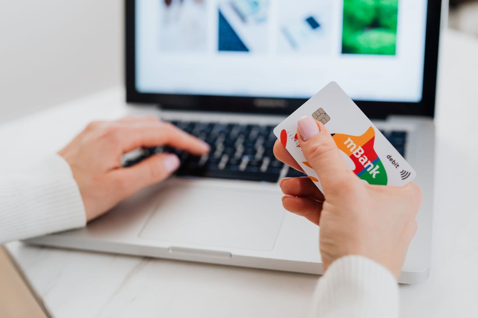 Hands holding a payment card beside a laptop