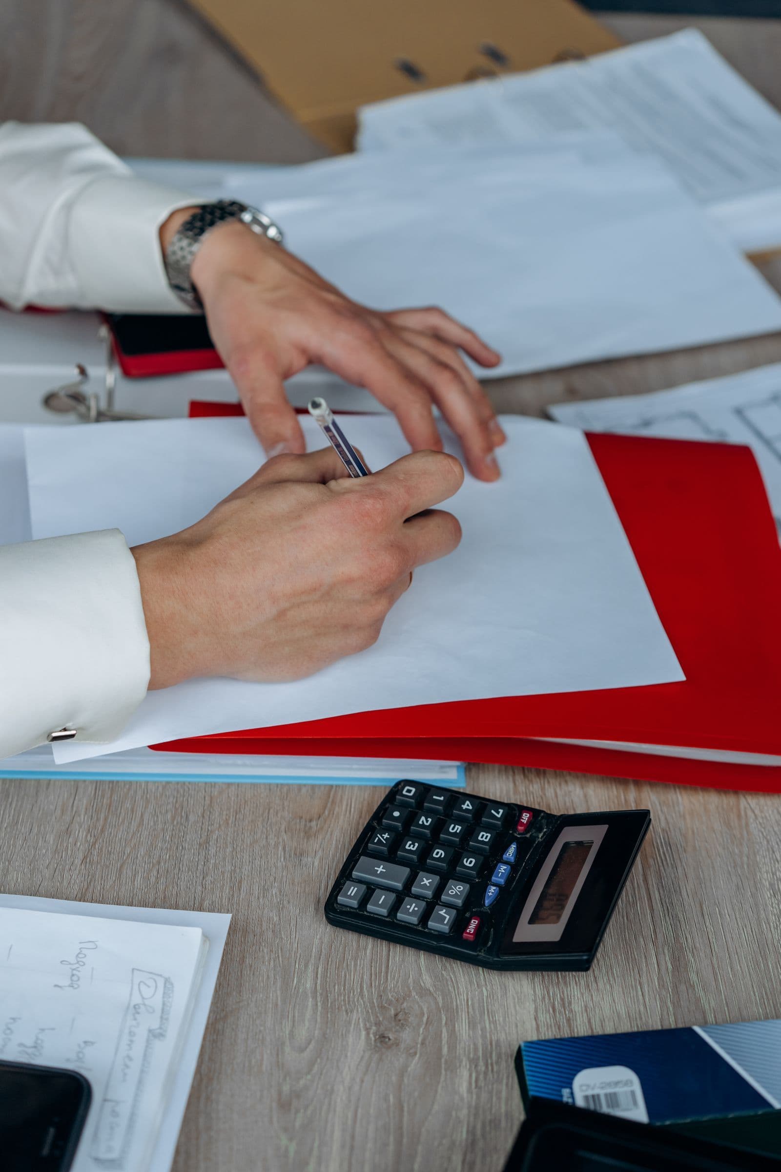 Hands checking paperwork beside a calculator