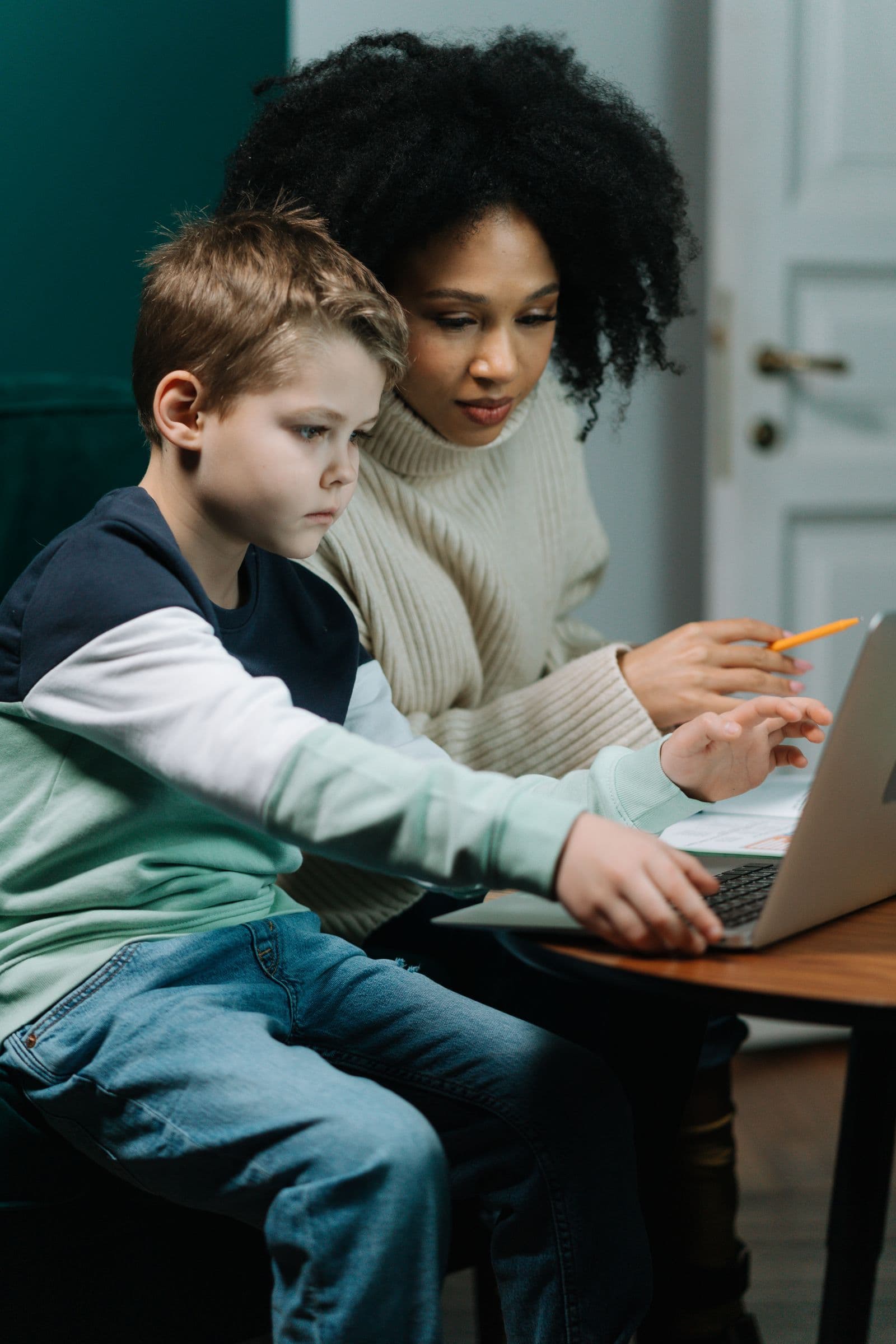 An adult helping a child work with a laptop and notebook