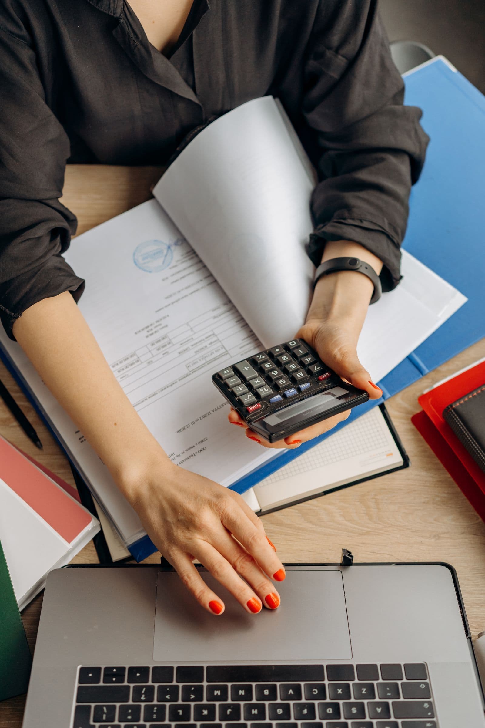 Hands using a calculator beside a laptop and documents