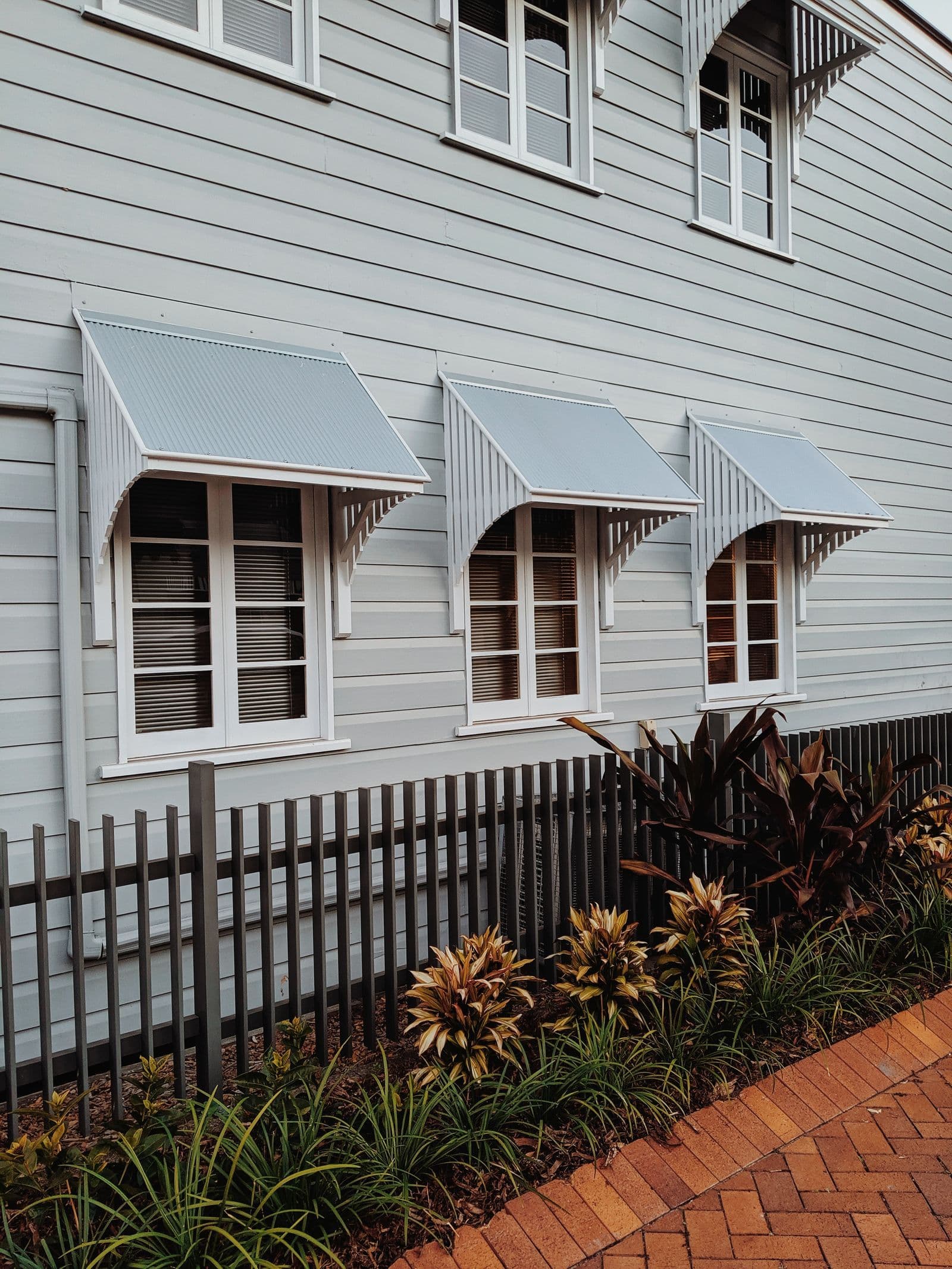 Exterior of a timber house with window awnings and garden plants